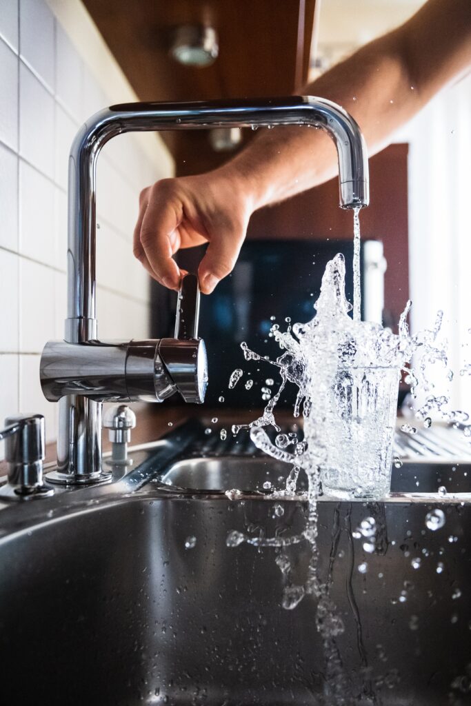 A glass being filled with water of the tap whilst the water is splashing everywhere.