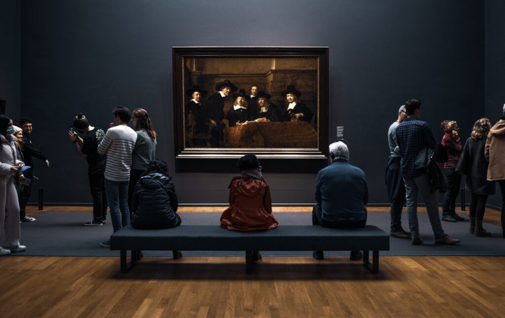 People sitting in front of a Rembrandt painting at the rijkmuseum in Amsterdam at night.