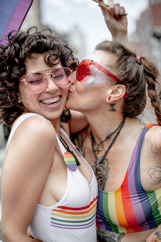 One person kissing the other one on the cheek during a gay pride. 