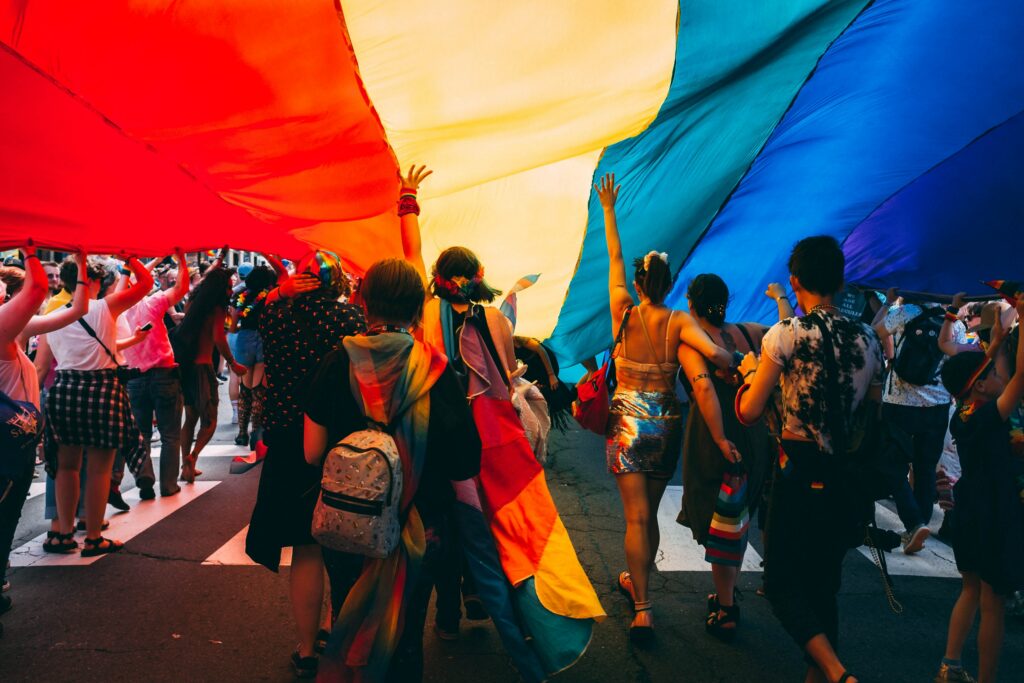 People marching under a big rainbow flag during a gay pride.